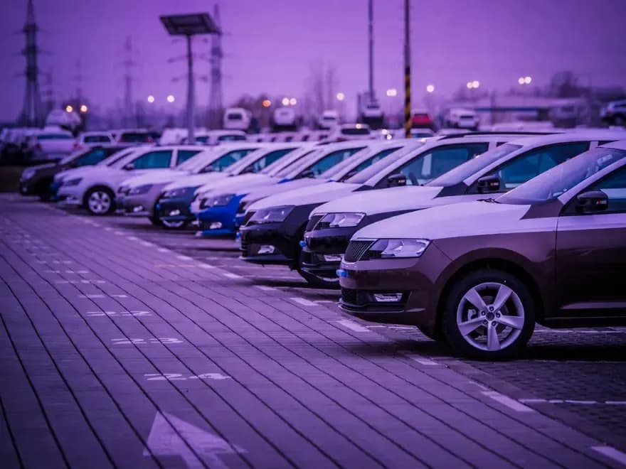 Fila de carros estacionados sob iluminação roxa em pátio, representando estoque automotivo e análise estratégica de como calcular custo de carro parado na operação comercial.