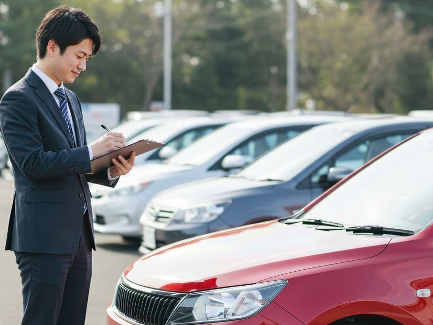 Avaliador profissional de terno examinando estoque de veículos para determinar como vender carro usado com precisão técnica.