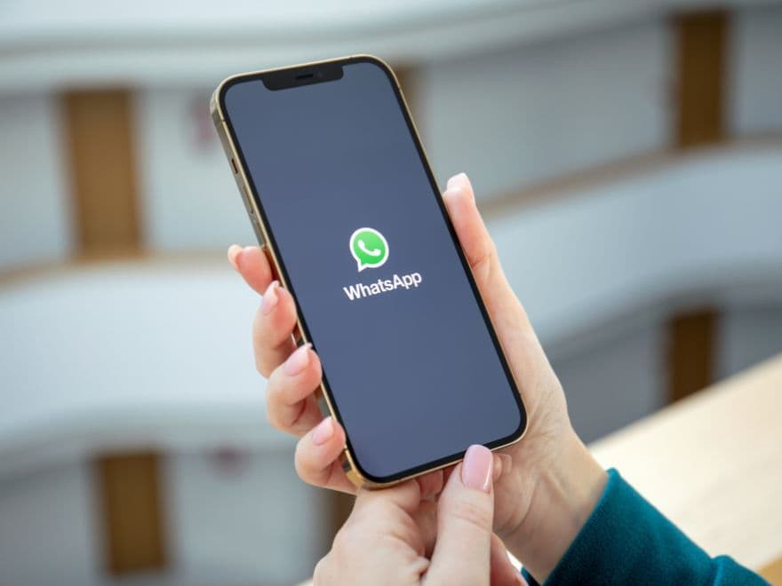 Mãos segurando um smartphone com o aplicativo WhatsApp aberto em um ambiente corporativo, simbolizando a importância da automação de vendas no WhatsApp.