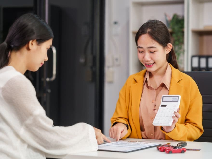 Consultora de vendas em concessionária mostrando cálculos em uma calculadora para cliente, representando a eficiência da automação de vendas no WhatsApp na agilidade de propostas.